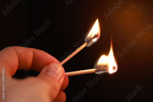 Obraz na plátně Closeup of a hand holding two burning match sticks on a black background with co