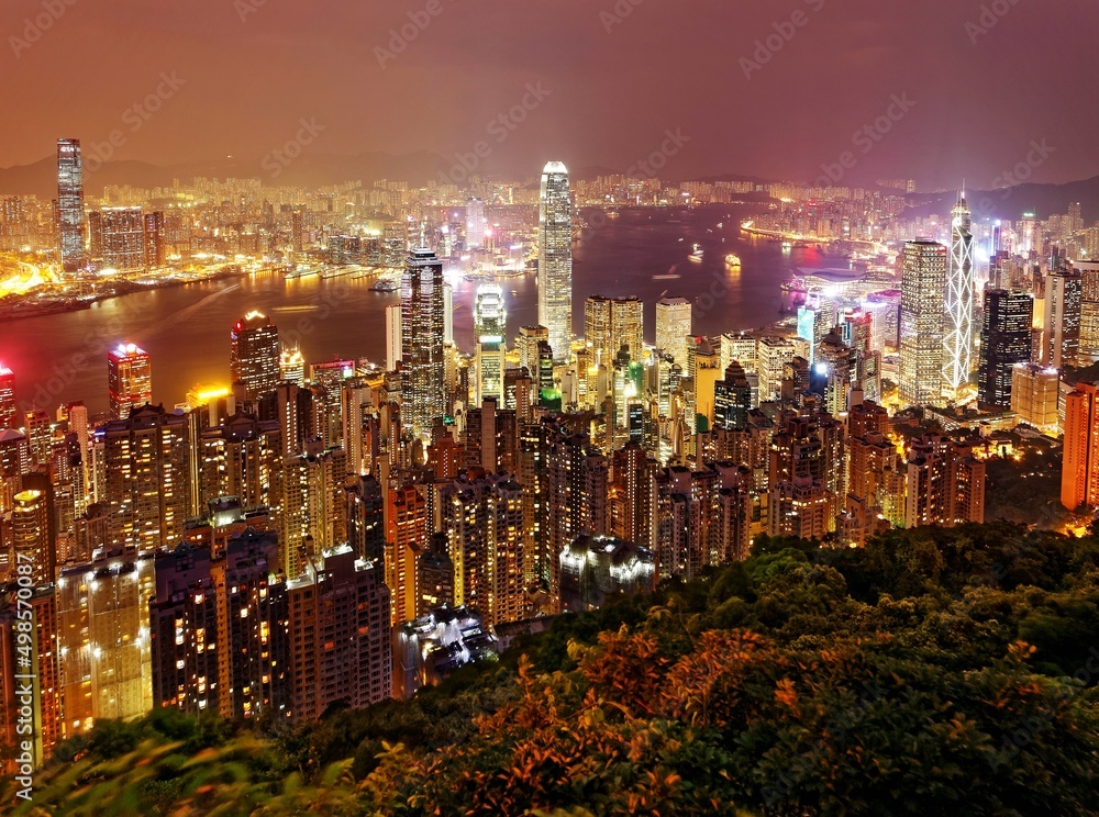 Naklejka premium Night scenery of Hong Kong viewed from top of Victoria Peak with city skyline of crowded skyscrapers along Victoria Harbour and Kowloon area across seaport ~ Beautiful cityscape of Hongkong at sunset