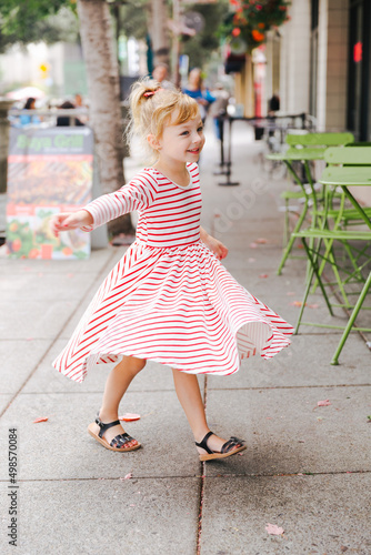 young girl in a striped dress twirling on the sidewalk next to a cafe