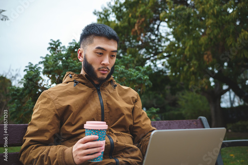 Serious ethnic freelancer working on laptop and drinking coffee photo