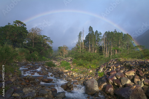Tropical landscape image showing a stream framed by a rainbow after a rainstorm. Image taken in Boquete, Panama.