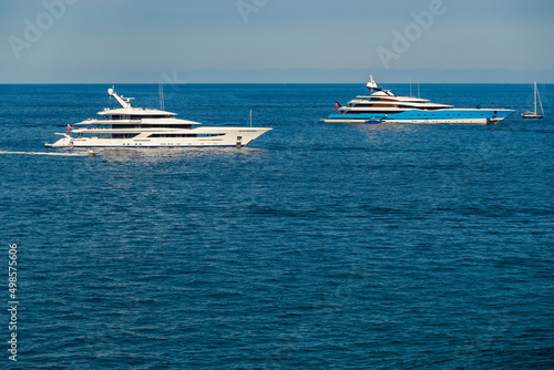 The two huge mega yachts are moored in sea at sunny day  the chrome plated handrail  sun reflection on glossy board of the motor boat