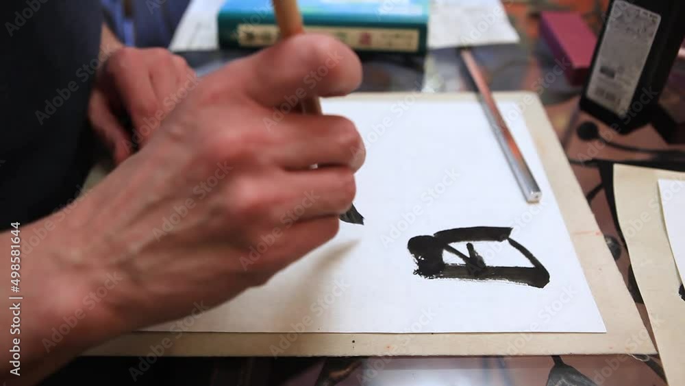 Close-up of a hand and a calligraphy brush. A man writes with a calligraphic brush with black ink on a white sheet of paper the phrase - every day is a good day Close-up of a hand and a calligraphy brush. A man writes with a calligraphic brush with black ink on a white sheet of paper the phrase - every day is a good day