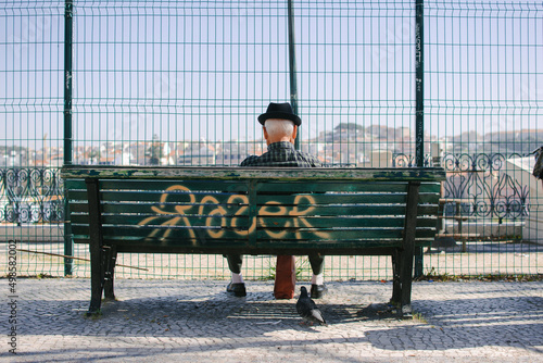 Canvas Print Old solitary male sitting on a bench facing away overlooking the city of Lisbon,