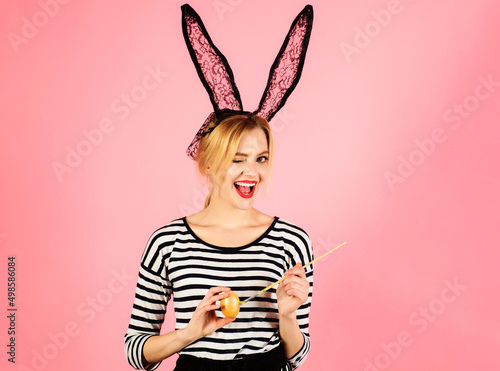 Happy easter day. Winking girl painting egg. Bunny woman in black lace rabbit ears. Spring holidays.