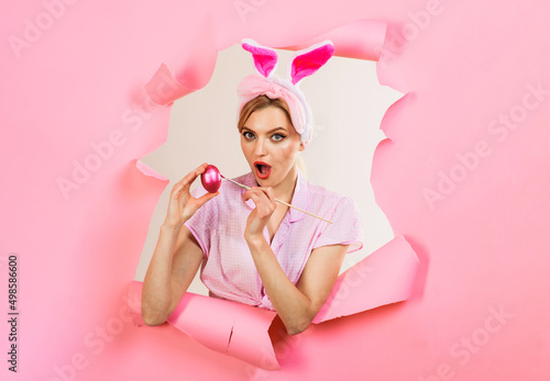 Surprised bunny girl painting Easter eggs. Rabbit woman looking through paper hole. Easter egg ideas.