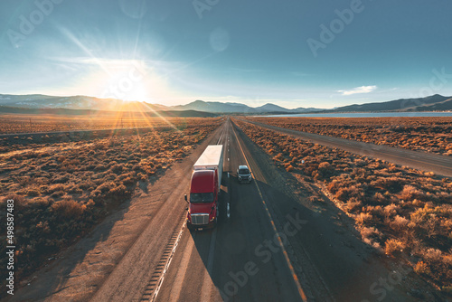 Drone shot of a truck driving on the highway in the sunset.