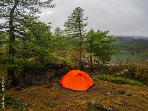 Orange tent under the rain. Camping on a autumn high-altitude plateau. Peace and relaxation in nature. Upper Shavlin Lake in the Altai.