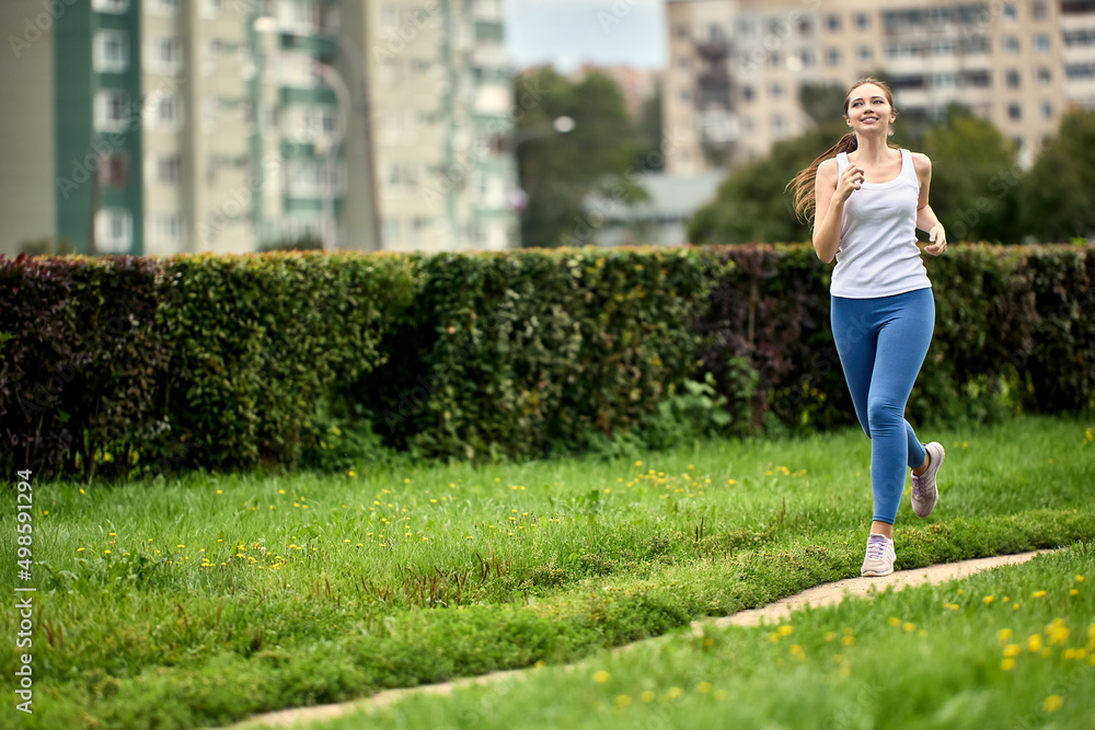 Jogging in summer in city park by happy young woman in sportswear.