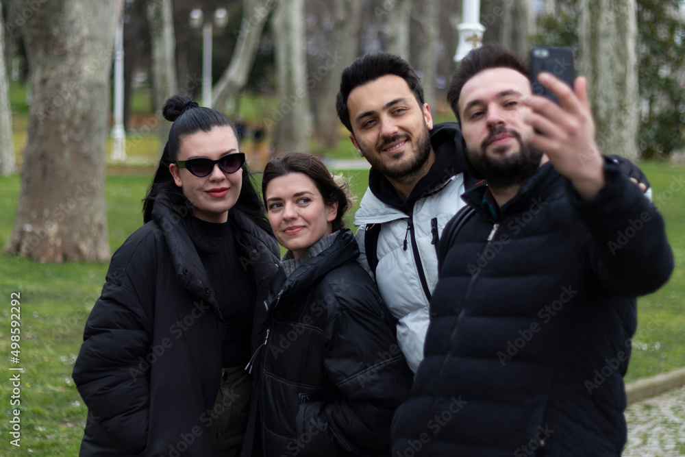 Four people taking selfie with smart phone. Green outside background. Friendship, close friends,  fun, joy and smile concept.