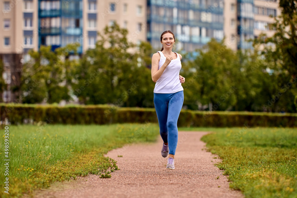 Jogging in summer in city park by happy woman in sportswear.