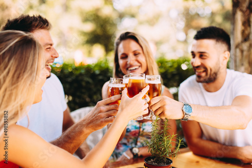 Group of happy friends toasting with beer in the backyard at a wooden table. Selective focus on beer