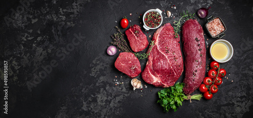 Set of fresh raw beef steak with spices ready to cook on a dark background. Long banner format. top view