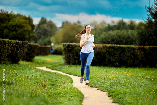 Running in city park by young woman in summer morning.