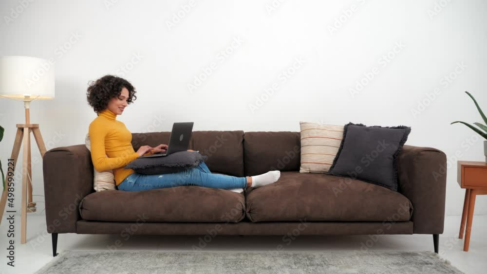 Smiling hispanic curly woman student study uses laptop typing on keyboard sitting on couch, distance education. Positive businesswoman works for computer online chatting with company employees at home Smiling hispanic curly woman student study uses laptop typing on keyboard sitting on couch, distance education. Positive businesswoman works for computer online chatting with company employees at home