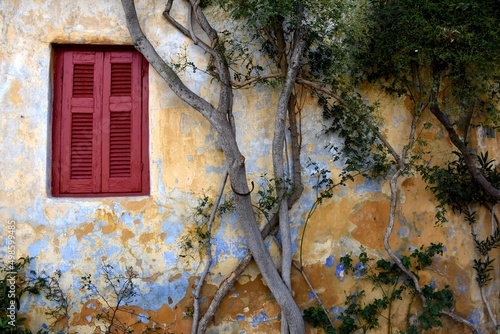 Exterior of yellow and blue house with red window and trees in Plaka, Athens, Greece