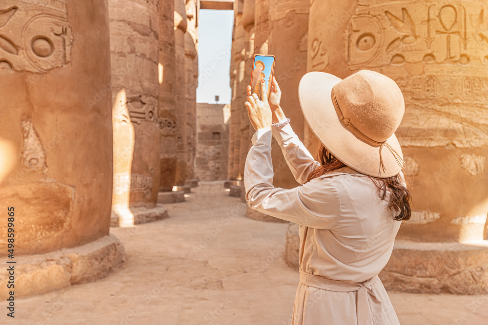 Travel blogger girl takes a pictures among columns of Hypostyle Hall at the ruins of the Karnak temple in the ancient city of Luxor in Egypt