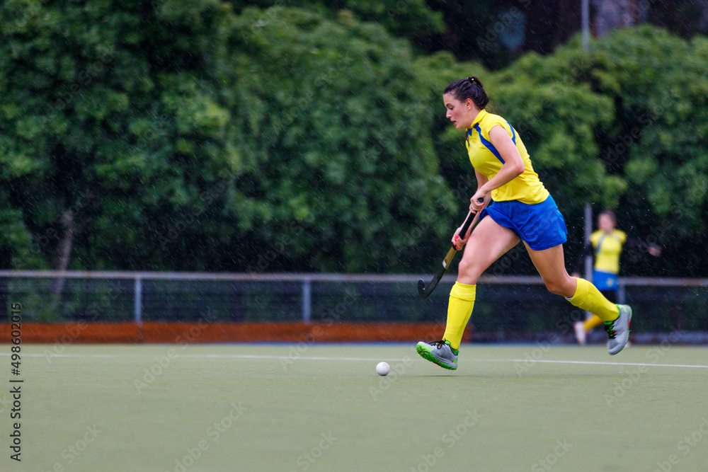 Young female field hockey player lead the ball in attack at heavy rain
