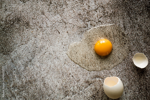 broken white farm fresh egg lies with shell and yolk on a gray neutral background