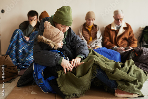 Billede på lærred Side view of young mother holding sleeping son while hiding in refugee shelter a