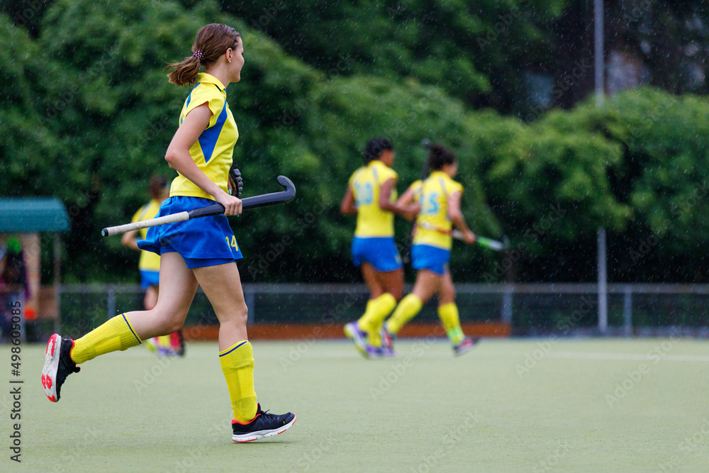Young teenage girl running on the pitch during the field hockey game in rain