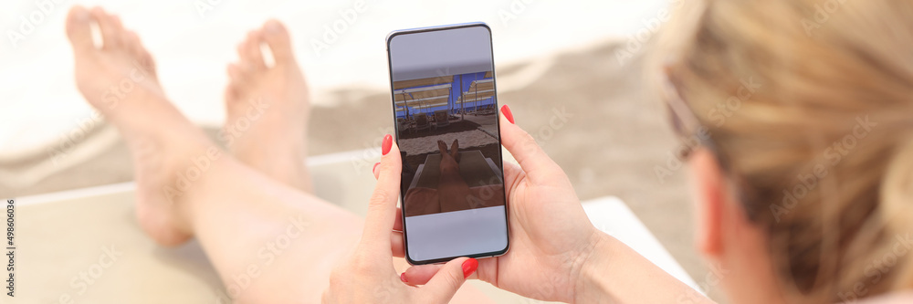 Φωτογραφία Young woman lying on sun lounger on beach and taking pictures of her feet on mob