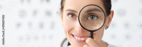 Woman optometrist holding magnifying glass in eyes against background of vision examination table