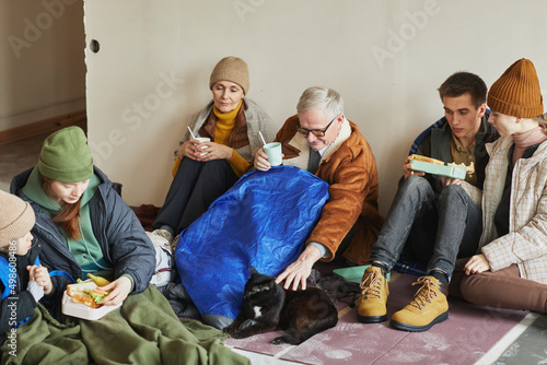 Canvas Print Group of Caucasian refugees eating food while hiding in shelter on floor covered