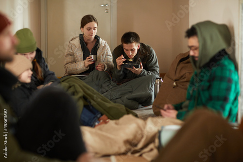 Portrait of Caucasian young couple eating simple food while hiding in refugee shelter with group of people