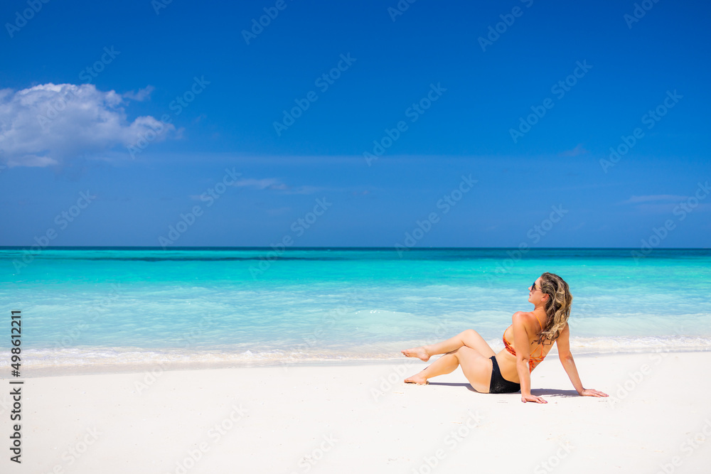Woman relaxing on the beach. Sexy bikini body legs, sunglasses woman enjoying paradise tropical beach. Exotic shore, sea water as freedom concept. Beautiful carefree fit body girl on travel vacation