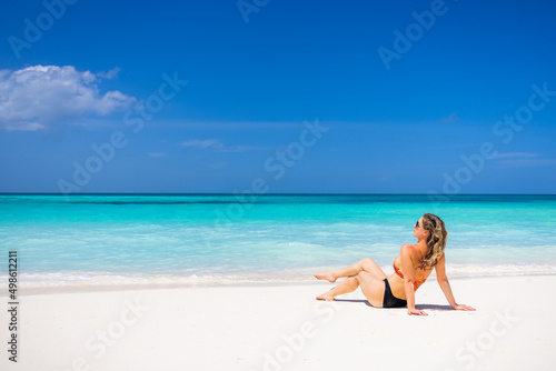 Woman relaxing on the beach. Sexy bikini body legs, sunglasses woman enjoying paradise tropical beach. Exotic shore, sea water as freedom concept. Beautiful carefree fit body girl on travel vacation