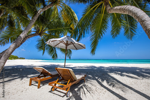 Beautiful tropical island scenery, two sun beds, loungers, umbrella under palm tree. White sand, sea view with horizon, idyllic blue sky, calmness and relaxation. Inspirational beach resort hotel 