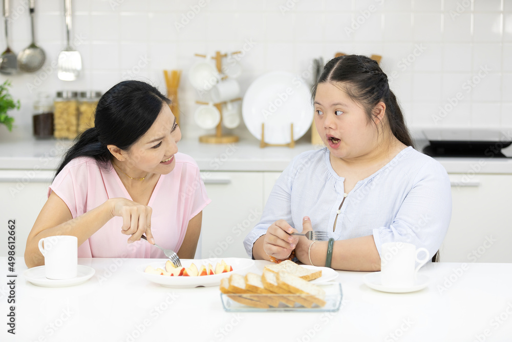 mother with down syndrome teenage girl or her daughter, eating apple together in a kitchen mother with down syndrome teenage girl or her daughter, eating apple together in a kitchen