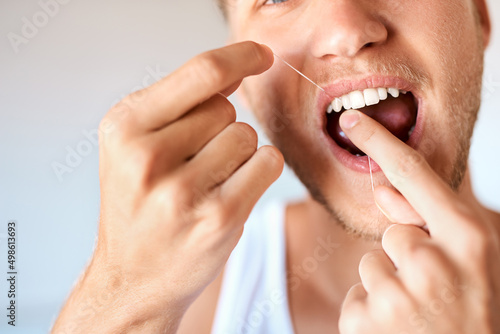 Up your dental hygiene game. Closeup shot of a young man flossing his teeth at home.