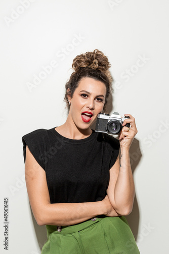 Studio shot of proud young girl with perfect light brown skin and beautiful curly hair in empowerment pose with a camera in hands on a white background. photo