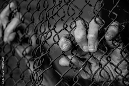 Fotografia Old female hands hold on to a rusty fence in the dark, Ukrainian prisoners in th