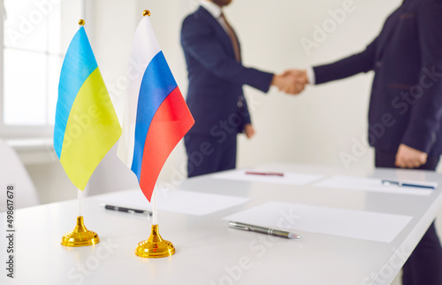 Russian Federation and Ukraine state representatives exchange handshakes over negotiation table with national flags. Successful diplomacy, signing peace treaty, ending conflict, stopping war concept