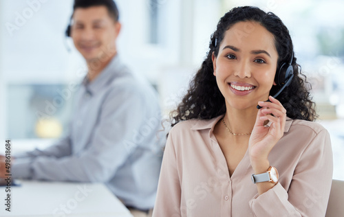 Call us and well take care of it. Portrait of a young call centre agent working in an office with her colleague in the background. photo