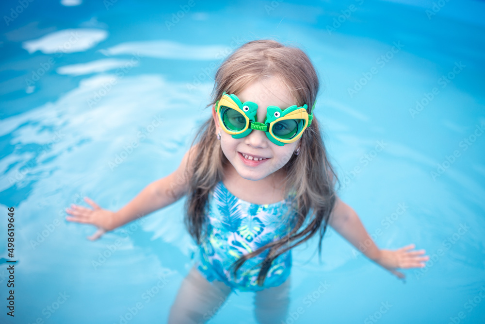 cute happy little girl in diving goggles and swimsuit. child learns to swim in the pool. training for children. concept kids sport, health, exercise, cooling in summer, kids beach fun