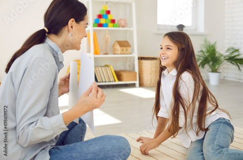 Professional therapist talking to happy child. Little girl having fun during lesson with private tutor or appointment with psychologist. Female English language teacher showing pictures to smiling kid