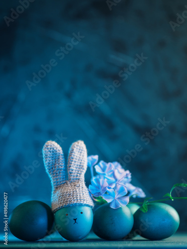 Easter eggs on a blue background. Crocheted hat with bunny ears. Copy space