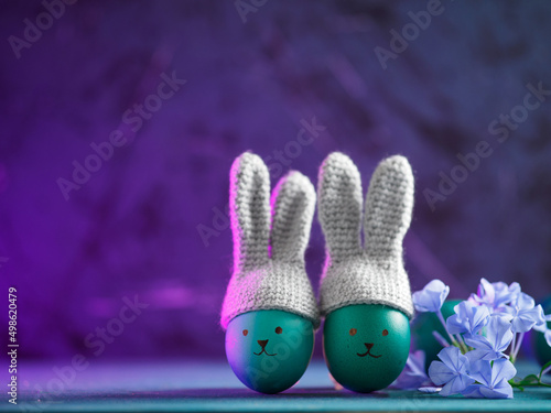 Blue eggs in crocheted hats with bunny ears. Neon purple background, copy space