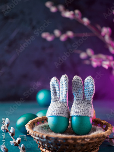 Easter eggs in a basket on a neon purple background. Willow branches. Vertical photo