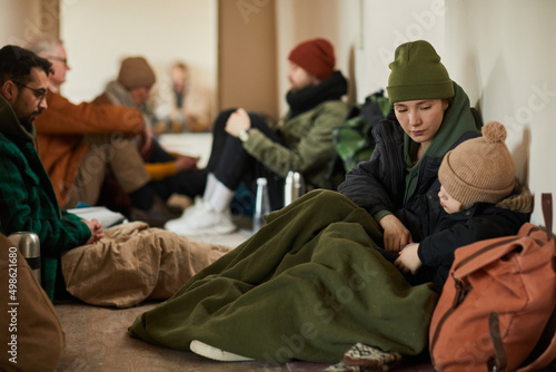 Caucasian young mother with child in refugee shelter sitting on floor and covered with blankets trying to keep warm photo