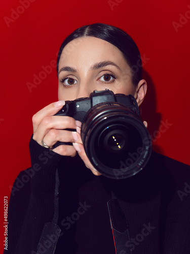 portrait brunette woman photographer with a camera on a red background.