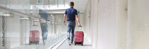Man with suitcase walking down in hotel corridor back view