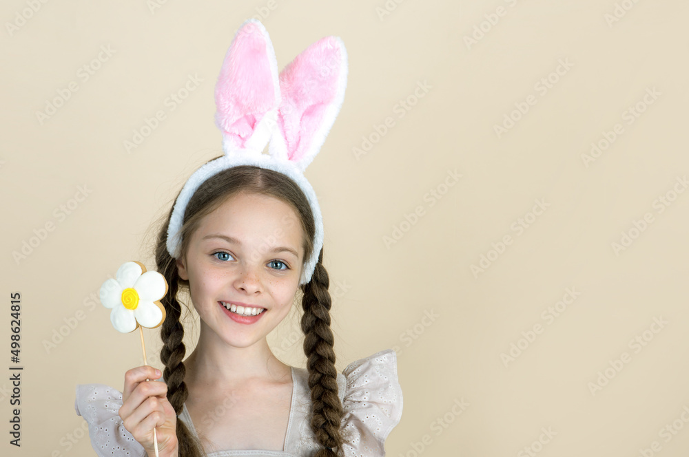 Smiling little girl with funny bunny ears holds flower cookie. Easter and Spring concept