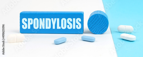 On a white and blue surface are pills, a pen and a wooden sign with the inscription - Spondylosis photo