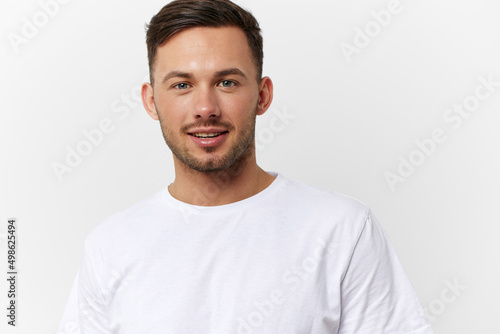Cheerful cute happy young tanned handsome man in basic t-shirt smile at camera posing isolated on over white studio background. Copy space Banner Mockup. People emotions Lifestyle concept. Portrait © SHOTPRIME STUDIO