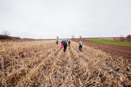 Group of hikers with backpacks walking on the rural trail. Active people outdoor. Healthy lifestyle. Cloudy spring day. Back view. Unrecognizable people. 